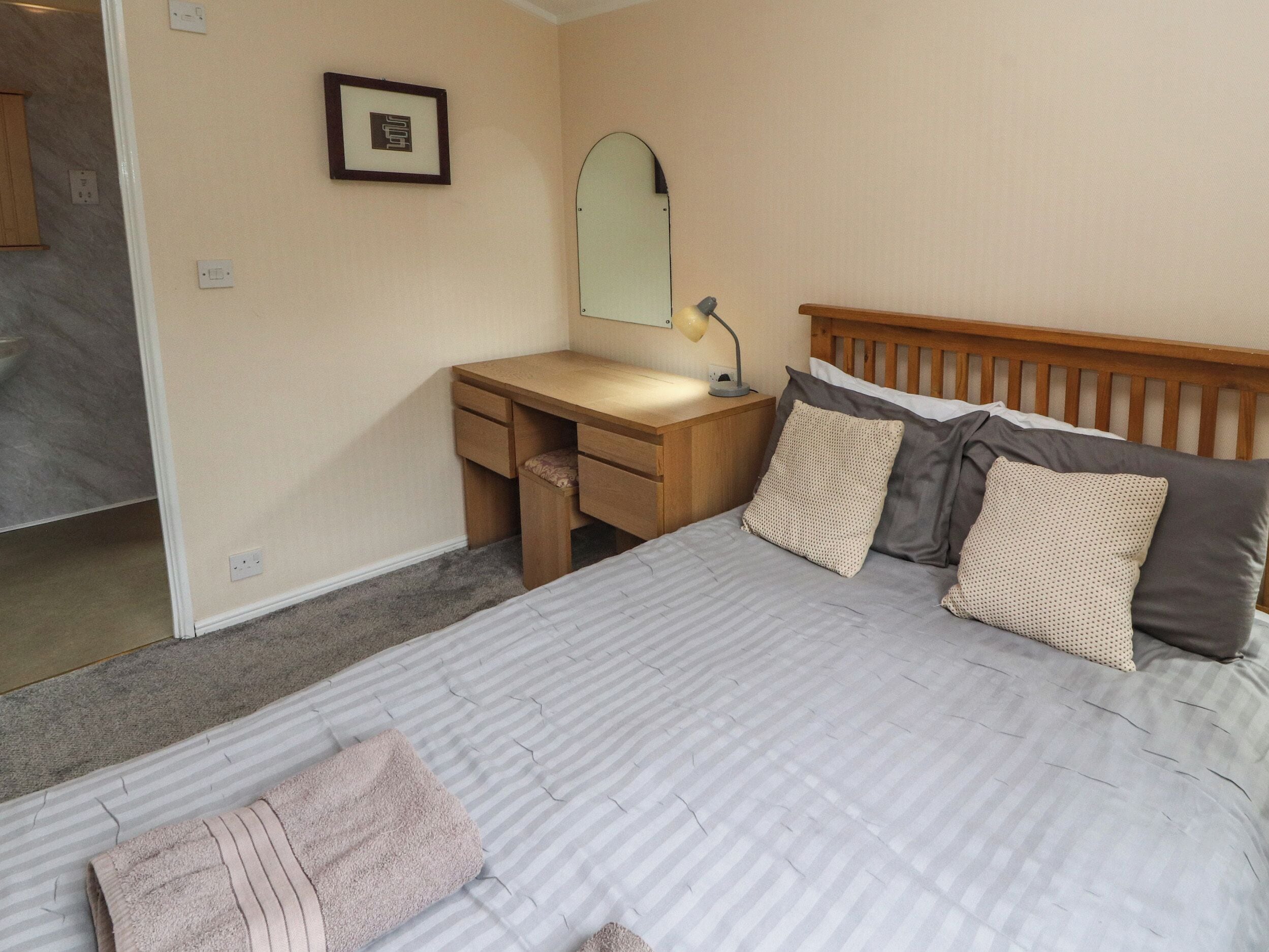 A bedroom with a bed, a desk, a mirror, and a nightstand.