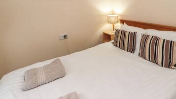 A neatly made bed with striped pillows and a white blanket, a bedside lamp, and a wall-mounted power outlet.