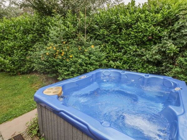 A hot tub in a backyard with a wooden deck and lush greenery in the background. - Langdale Lodge 15 (Windermere)