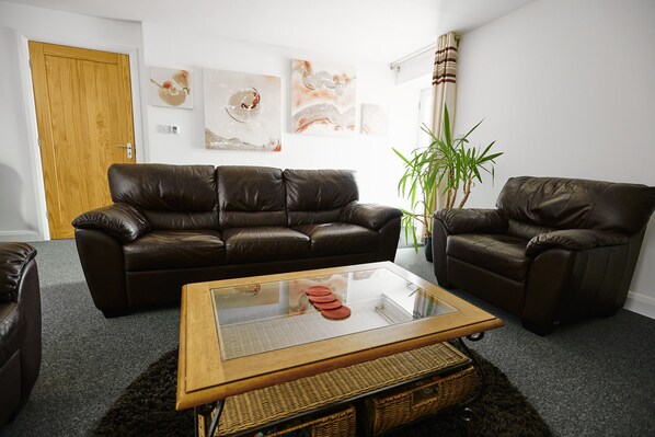 A living room with a brown leather sofa, a glass-top coffee table, and a potted plant. - Penyghent View (Settle)