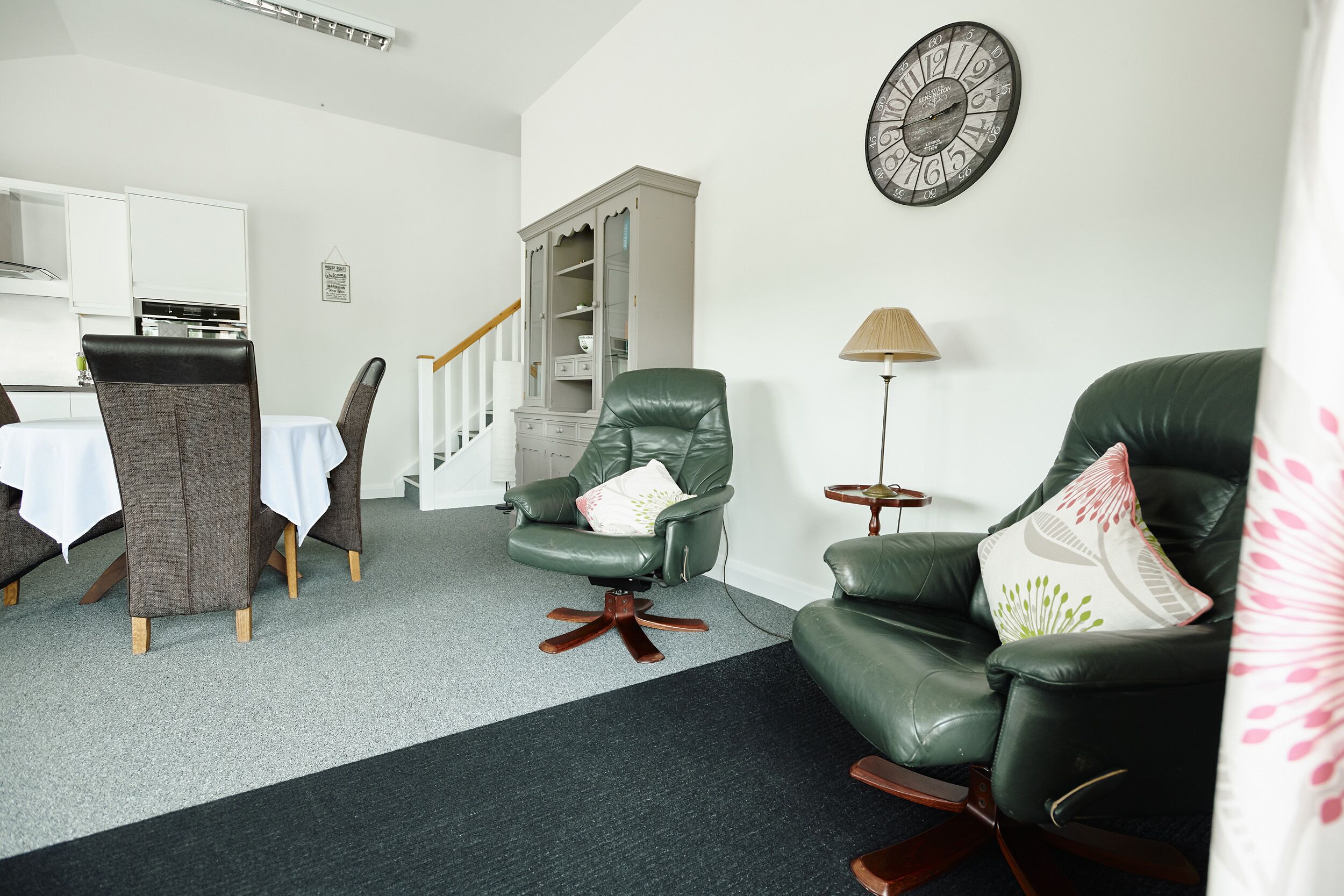 Un salon comprenant un coin repas, un fauteuil en cuir vert, un canapé, une lampe et une horloge murale.