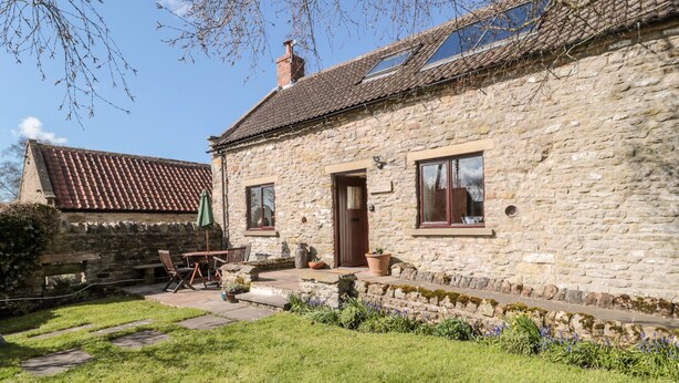 A stone house with a tiled roof, a wooden bench, and a small garden with flowers. - Dairy House (Pickering)