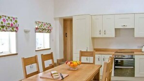 Un comedor con una mesa y sillas de madera, un frutero y una ventana con cortinas estampadas.