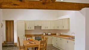 Una cocina compacta con armarios blancos, una mesa de comedor de madera y piso de baldosas.