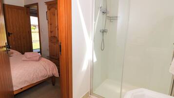 Un dormitorio con cama, armario de madera y zona de ducha con cristal.