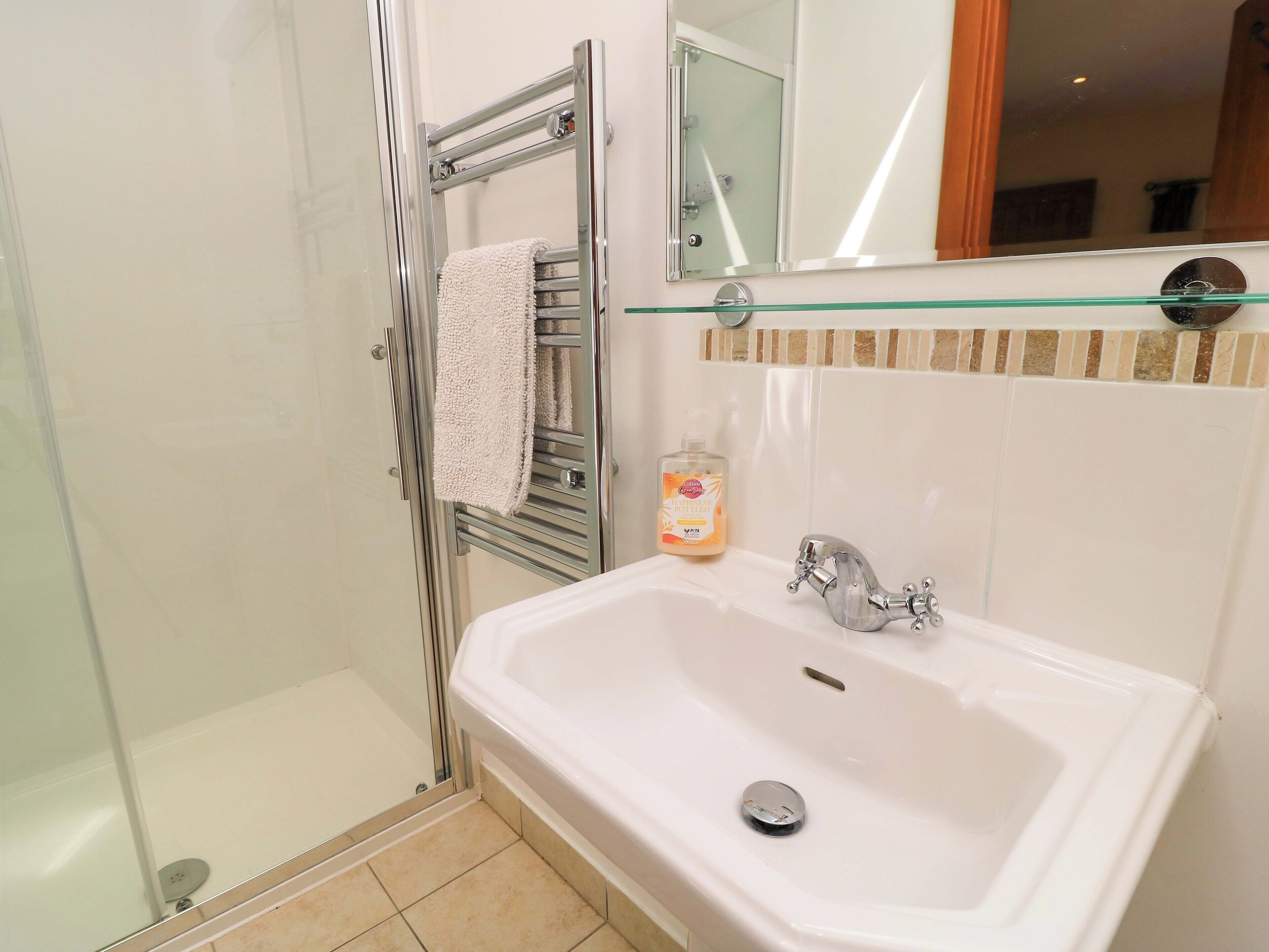 Un baño con cabina de ducha de vidrio, un lavabo blanco con grifo cromado y una botella de jabón para manos en la encimera.