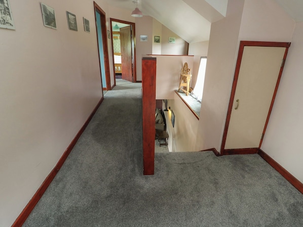 A hallway with a carpeted floor, wooden door frames, and a staircase leading to an upper level. - Glan y Gors (Caernarfon)