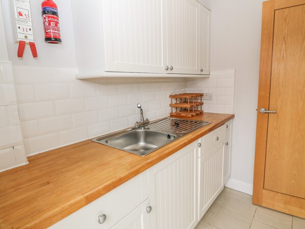 A kitchen with white cabinets, a stainless steel sink, and a wooden countertop. - 5 Cae Derwydd (Cemaes Bay)