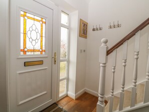 A white door with a stained glass window, a wooden staircase, and a wall-mounted picture frame. - 5 Cae Derwydd (Cemaes Bay)