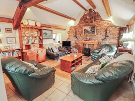 A cozy living room with leather sofas, a wooden coffee table, a stone fireplace, and a television.