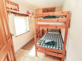 A bunk bed with a checkered bedspread and a green blanket, a window with curtains, and a wall-mounted shelf with candles and a picture.