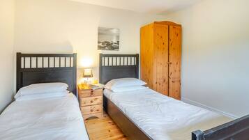 Quarto com duas camas de solteiro, cabeceiras de madeira, mesa de cabeceira com abajur e guarda-roupa de madeira.