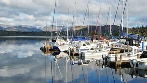 A marina with several boats docked, calm water, and mountains in the background. - Top Lodge, 4 Skiptory Howe (Windermere)