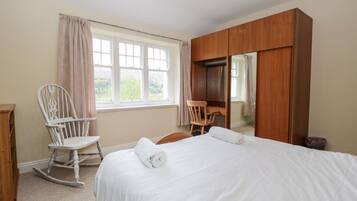 Un dormitorio con una cama, dos mecedoras, un armario de madera y una ventana con cortinas.