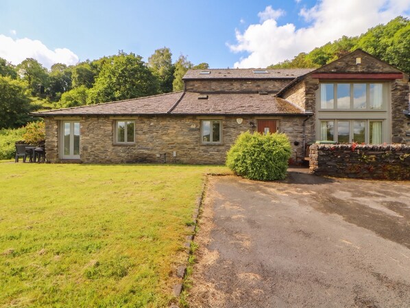 A stone house with a large lawn, a small garden, and a paved driveway.