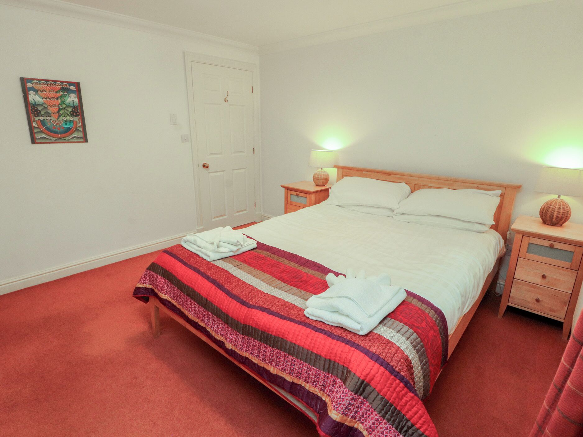 Une chambre à coucher comprenant un lit, deux tables de chevet, une porte et un élément décoratif mural.