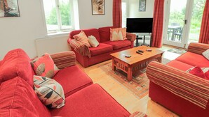 A living room with red sofas, a coffee table, a TV, and a large window with curtains. - Winster Fields (Windermere)