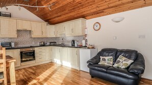 Eine kompakte Küche mit Holdekor-Schränken, einer Mikrowelle und einem Kühlschrank. Es gibt ein schwarzes Ledersofa mit Zierkissen sowie einen Holzesstisch mit Stühlen.