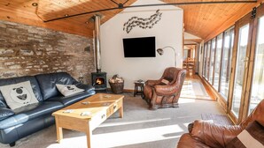 Ein gemütliches Wohnzimmer mit Steinwand, Kamin, Ledersofas und großen Fenstern.