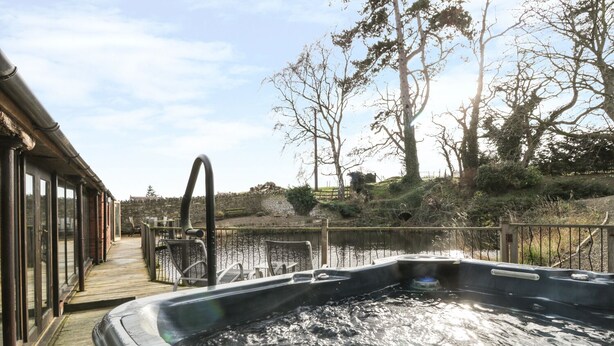 Ein Whirlpool mit Holzboden und Glasgeländern, umgeben von Bäumen und einer Steinmauer.