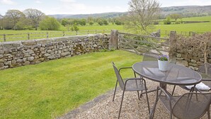 A stone wall with a wooden gate, a grassy lawn, and a metal table with chairs. - Reynard Ing Cottage (Ilkley)