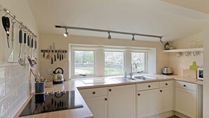 A modern kitchen with white cabinets, a black induction cooktop, a double sink, and a window providing natural light. - Reynard Ing Cottage (Ilkley)
