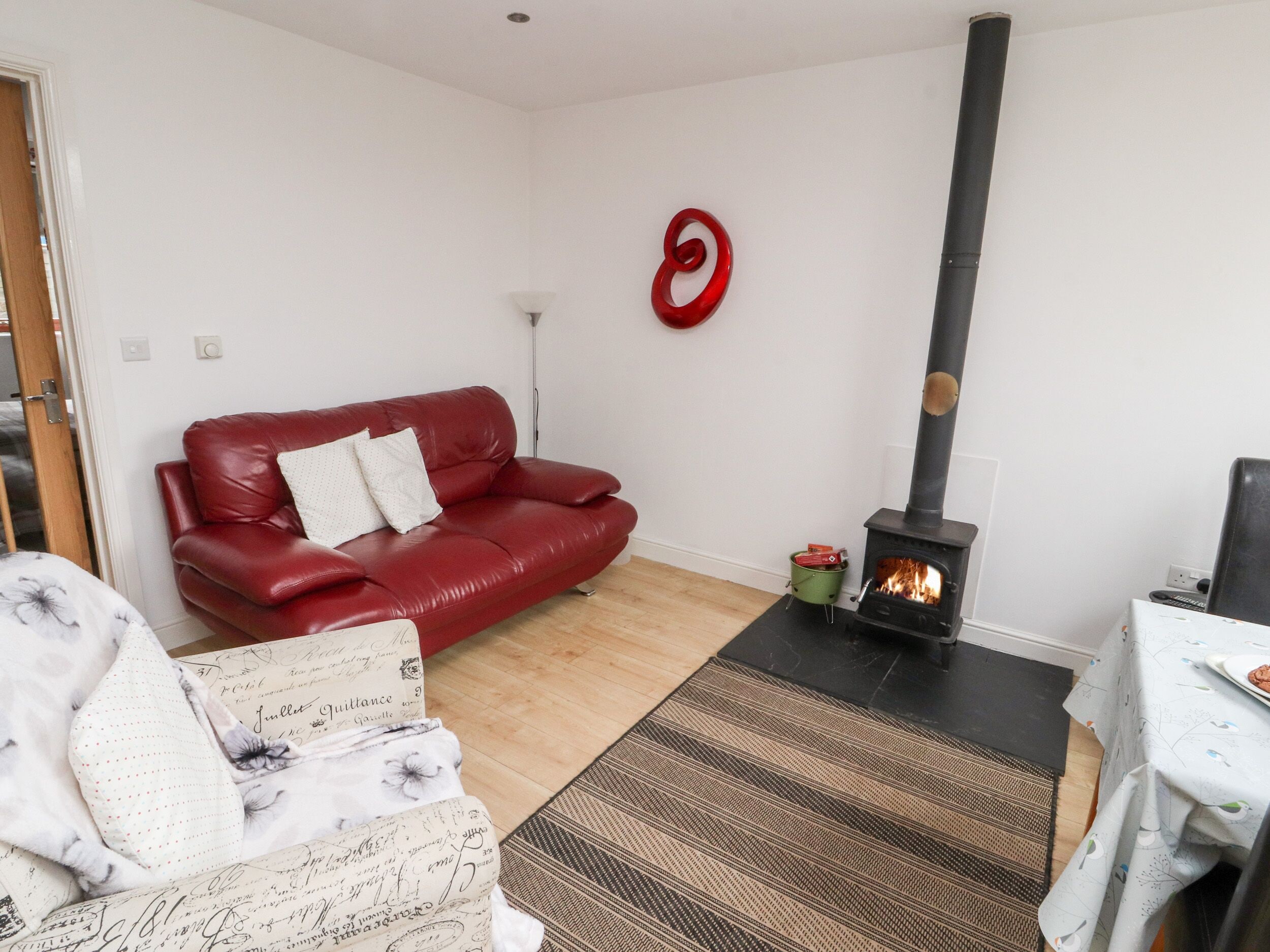 A living room with a red leather sofa, a patterned rug, a fireplace with logs, and a wall-mounted red circular decoration.