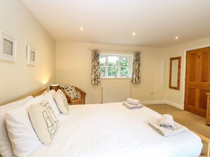 A bedroom with a large bed, a wooden chair, a window with curtains, and a door. - Oak Tree Lodge (Norwich)