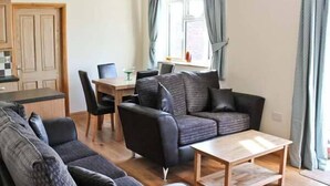 A compact living space with a sofa set, a dining table, and a kitchen area. - Moat Farm Cottage (Norwich)