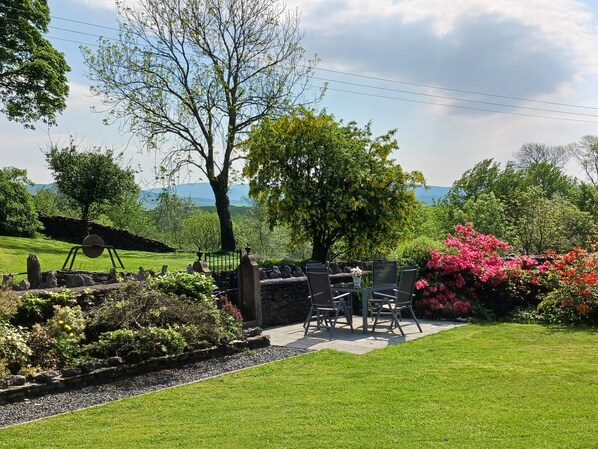 A well-maintained garden with a stone bench and table, surrounded by lush greenery and flowering plants.