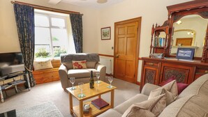 A living room with a sofa, a coffee table with wine glasses, a television, and a wooden cabinet with a mirror. - Longwell House (Kendal)