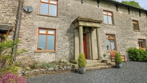 A stone building with a central entrance, multiple windows, and a gravel driveway. - Longwell House (Kendal)