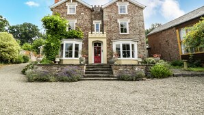 A two-story stone house with a red door, multiple windows, and a gravel driveway. - Wheelbarrow Castle (Leominster)