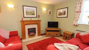 Una sala de estar con chimenea, televisor y sofás rojos.