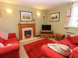 A living room with a fireplace, a television, and red sofas. - Barnbrook (Leyburn)