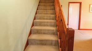 Una escalera alfombrada con barandillas de madera que conduce a una habitación con una puerta blanca y un cuadro en la pared.