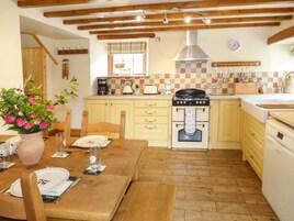 A cozy kitchen with wooden beams, a stove, and a dining table set for two.