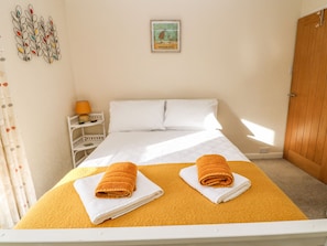 Quarto com cama, duas toalhas, mesa de cabeceira, abajur e um objeto decorativo na parede.