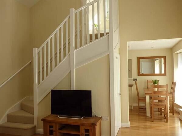 Un escalier avec des rampes blanches mène à un palier. Un téléviseur à écran plat est posé sur un meuble en bois, sur le palier.