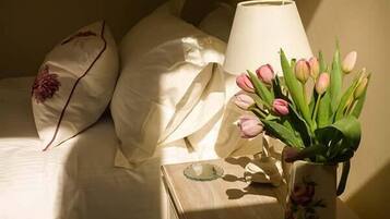 Ein Bett mit weißen Leinen und dekorativen Kissen, ein Nachttisch mit Lampe und Blumenvase.