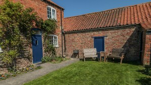A brick building with a red-tiled roof, a blue door, and a small garden area with a bench and table. - Bellafax Cottage (Malton)