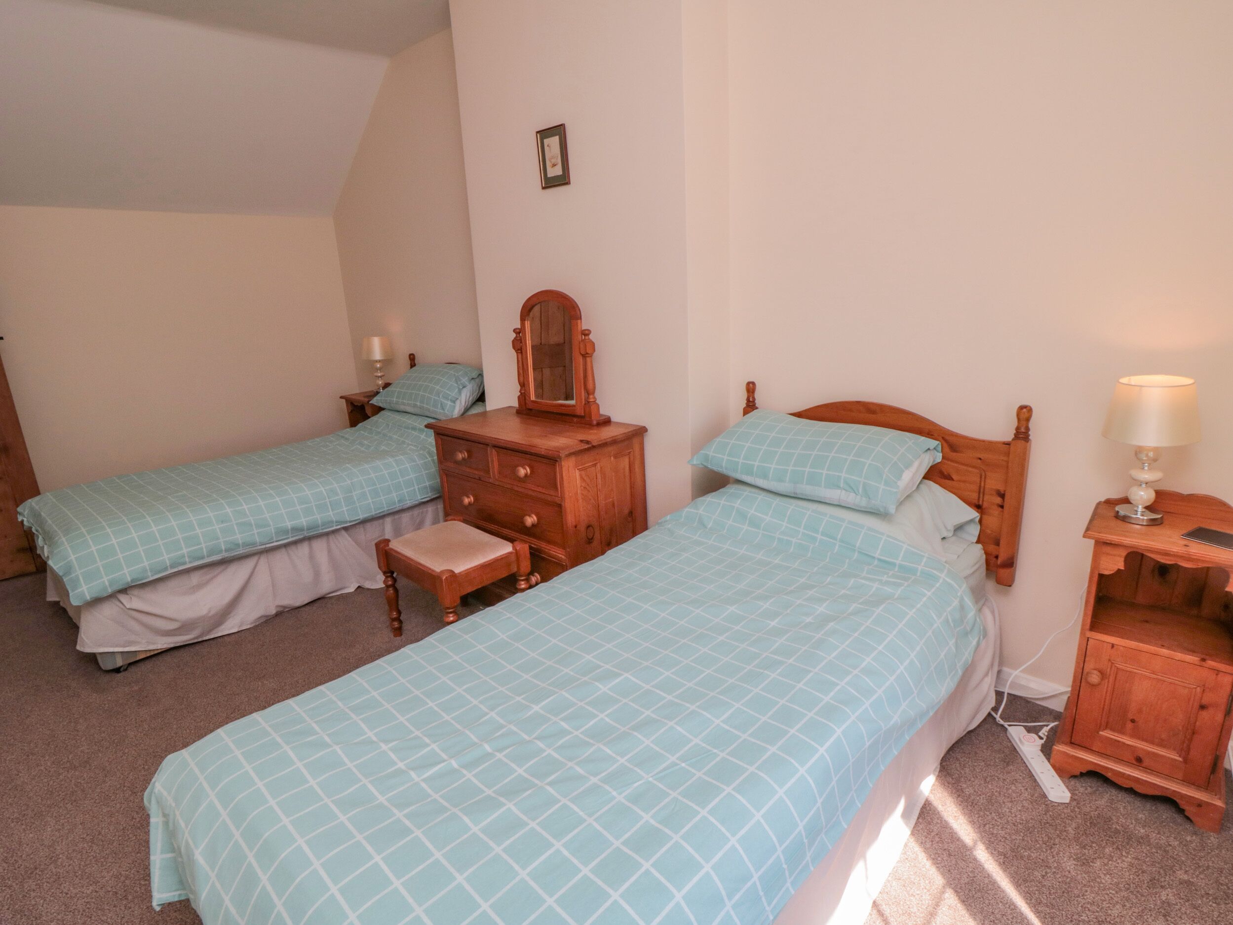 A bedroom with two single beds, a wooden dresser, a nightstand with a lamp, and a small table with a lamp.
