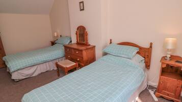 A bedroom with two single beds, a wooden dresser, a nightstand with a lamp, and a small table with a lamp.