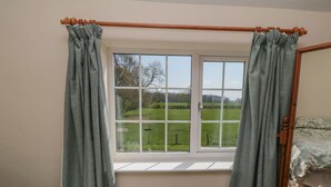 A bedroom with a window, a wooden bed frame, and a green bedspread. - Bellafax Cottage (Malton)