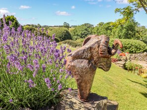 Un jardin agrémenté d’une sculpture d’éléphant posée sur un socle en pierre, entourée de plantes de lavande.