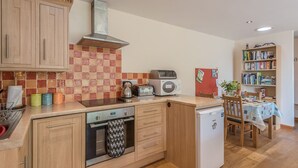 Eine kleine Küche mit Holzschränken, einer gefliesten Spritzschutzwand, einer Mikrowelle, einem Wasserkocher und einem kleinen Kühlschrank.