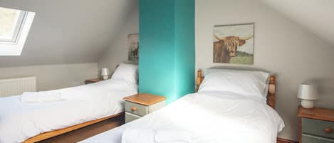 A bedroom with two single beds, a teal accent wall, a wooden headboard, a nightstand with a lamp, and a framed picture of a cow on the wall.