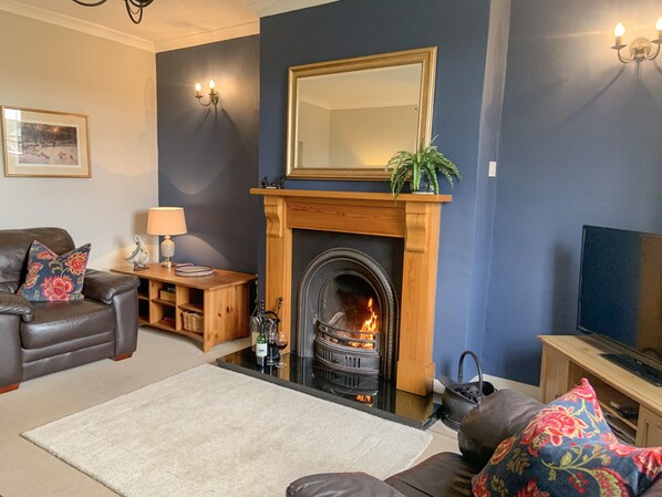 A living room with a fireplace, a leather sofa, a television, and a coffee table. - Miners Cottage (Barnard Castle)