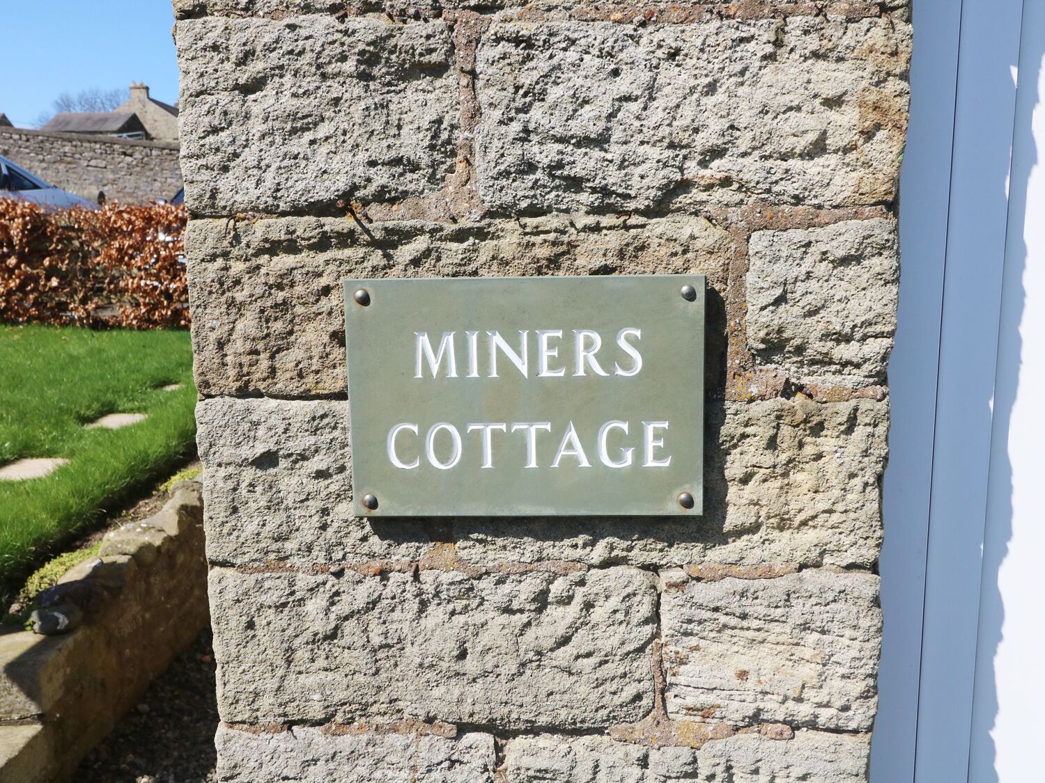 A sign on a stone wall that reads "Miners Cottage".