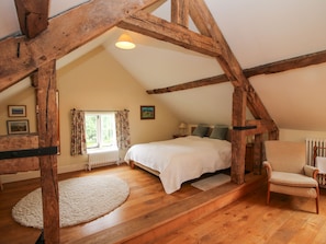 A cozy attic bedroom with exposed wooden beams, a bed, a chair, and a window with curtains. - Old Coach House (Shrewsbury)